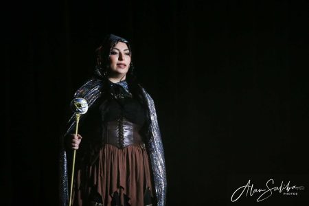 A performer dressed as a character in a pantomime, holding a prop on stage during a theatrical performance. An actress in costume performing in a pantomime show.