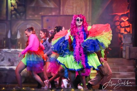 A lively performance from "Il-Mummja" with performers in bright, colourful costumes during a theatrical show. Vibrant scene from the pantomime "Il-Mummja" featuring performers in colourful costumes on stage.