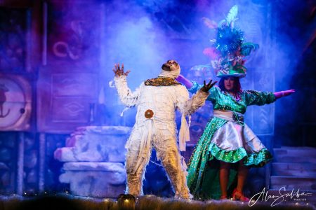 A lively scene from "Il-Mummja" pantomime showing performers in vibrant costumes on stage with dramatic lighting. Performers in a colourful pantomime scene with elaborate costumes and stage lighting.