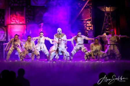 A group of actors dressed as mummies performing on stage in a colourful, theatrical setting. Performers in costume during a theatrical pantomime scene.