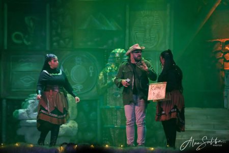 Actors enact a humorous scene on stage with themed costumes and set design. Performers in costume during a pantomime scene.