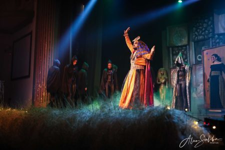 A scene from the pantomime "Il-Mummja" showcasing actors in costume during a theatrical performance. Actors performing in a theatrical play on stage with costumes and lighting.