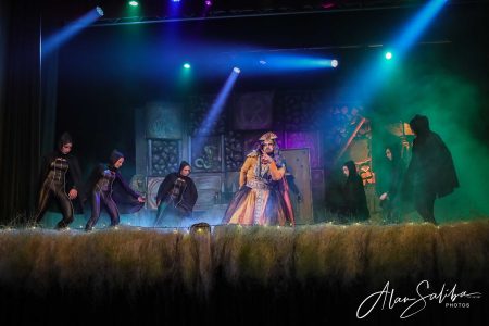 A theatrical scene from "Il-Mummja" featuring actors in costumes on stage with colourful lighting. Performers in costume during a theatrical pantomime scene.
