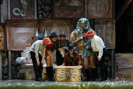 A group of performers in costume gather around a treasure chest on stage during a pantomime performance. Treasure chest scene from the pantomime "Il-Mummja" at Fondazzjoni Teatrali Silvio Fleri Soler.