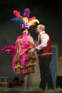 A performer dressed as Zorro in colourful costume with feathers, engaging with a man on stage during a pantomime show. Zorro Pantomime Performance.