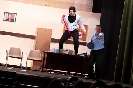 A lively scene from a theatrical performance featuring two actors in humorous poses, set in a theatre environment. Actors performing a comedic scene on stage during a theatrical play.