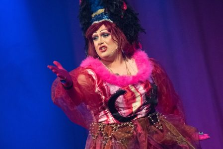 A performer in elaborate costume and makeup delivering a dramatic act during a theatrical show. Actress in vibrant theatrical costume performing on stage.