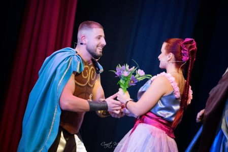 A male and female actor exchange flowers during a scene at the Fondazzjoni Teatrali Silvio Fleri Soler. Actors performing on stage during a theatrical play.
