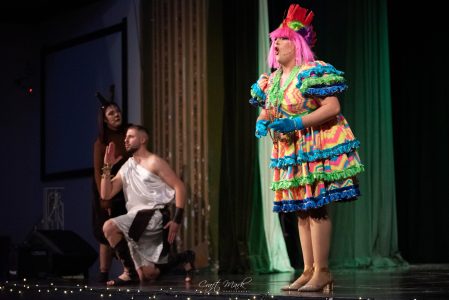 The image shows actors in elaborate costumes during a theatrical performance at the theatre. A colourful theatrical scene with performers in vibrant costumes on stage.