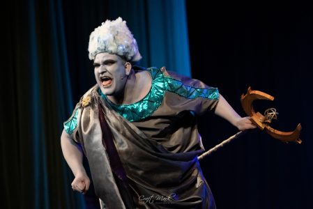 A performer in elaborate costume and makeup passionately acting during a theatrical production. Actor in dramatic costume performing on stage with intense expression.