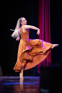 A dancer in a flowing orange dress performs a graceful move on stage during a dance show. Elegant dancer in a flowing orange dress performing on stage.
