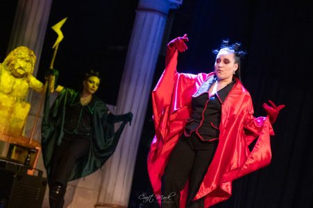 Two actors in colourful costumes performing on stage with classical columns in the background. Performers in vibrant costumes on stage during a theatrical show at Fondazzjoni Teatrali Silvio Fler.