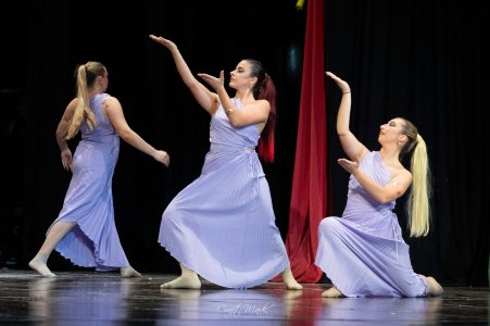 Three dancers in lavender costumes performing on stage with black background. Dancer performance at Fondazzjoni Teatrali Silvio Fleri Soler.