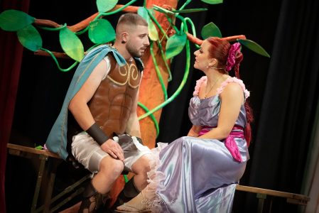 Two actors in costume engaging in a scene from a theatrical production set in a forest environment. Actors performing in a theatrical play on stage with forest backdrop.