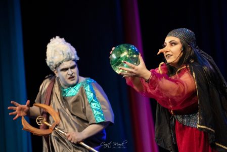 Two actors in elaborate costumes performing a scene during a theatrical production at Fondazzjoni Teatrali Silvio Fleri Soler. Actors performing a theatrical scene on stage with costumes and props.
