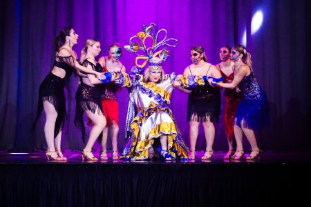 A lively performance of "Korps Brajd" with dancers and a central performer in vibrant costume on stage. An energetic scene from the pantomime "Korps Brajd" featuring dancers and a performer in elaborate c.
