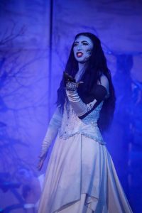 A performer in costume during a theatrical pantomime, with a mystical forest background. Enchanted Forest performer in costume with dramatic makeup and flowing dress.