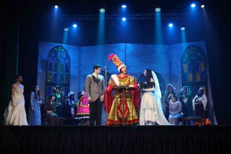 A lively stage scene from the Korps Brajd pantomime, featuring actors in vibrant costumes and set against a theatrical backdrop. Performers in colourful costumes during a theatrical pantomime scene.