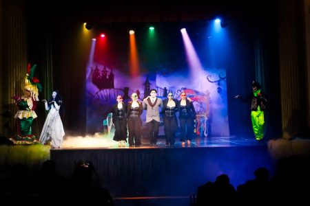 A lively scene from a pantomime performance featuring actors in vibrant costumes on stage. Performers on stage during a pantomime show with colourful costumes and stage lighting.
