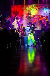 Vibrant performance with actors in elaborate costumes during the Korps Brajd pantomime. An energetic scene from the pantomime featuring performers in colourful costumes on stage.