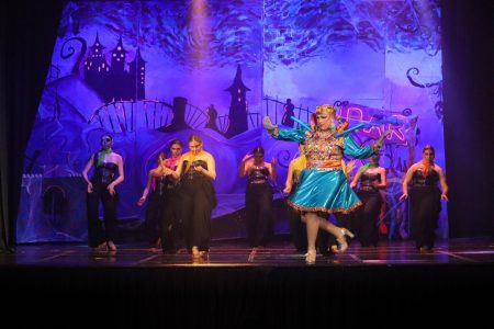A lively theatrical performance with dancers and a colourful clown in front of a whimsical backdrop. Vibrant pantomime scene featuring performers in colourful costumes on stage.